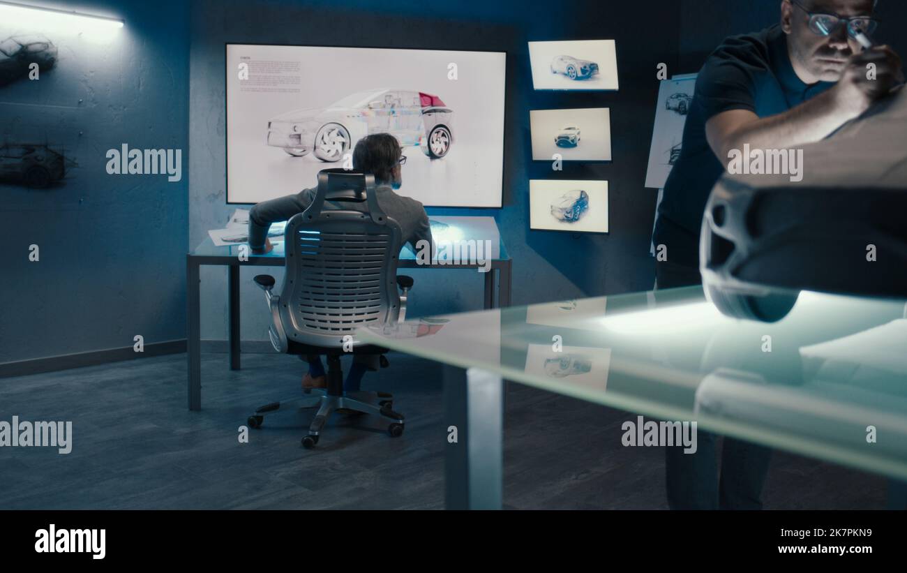 Les ingénieurs et les concepteurs automobiles travaillent dans une usine automobile innovante de haute technologie. Fabrique une voiture prototype à la pointe de la technologie. Le concepteur utilise la table de l'écran tactile numérique. Banque D'Images