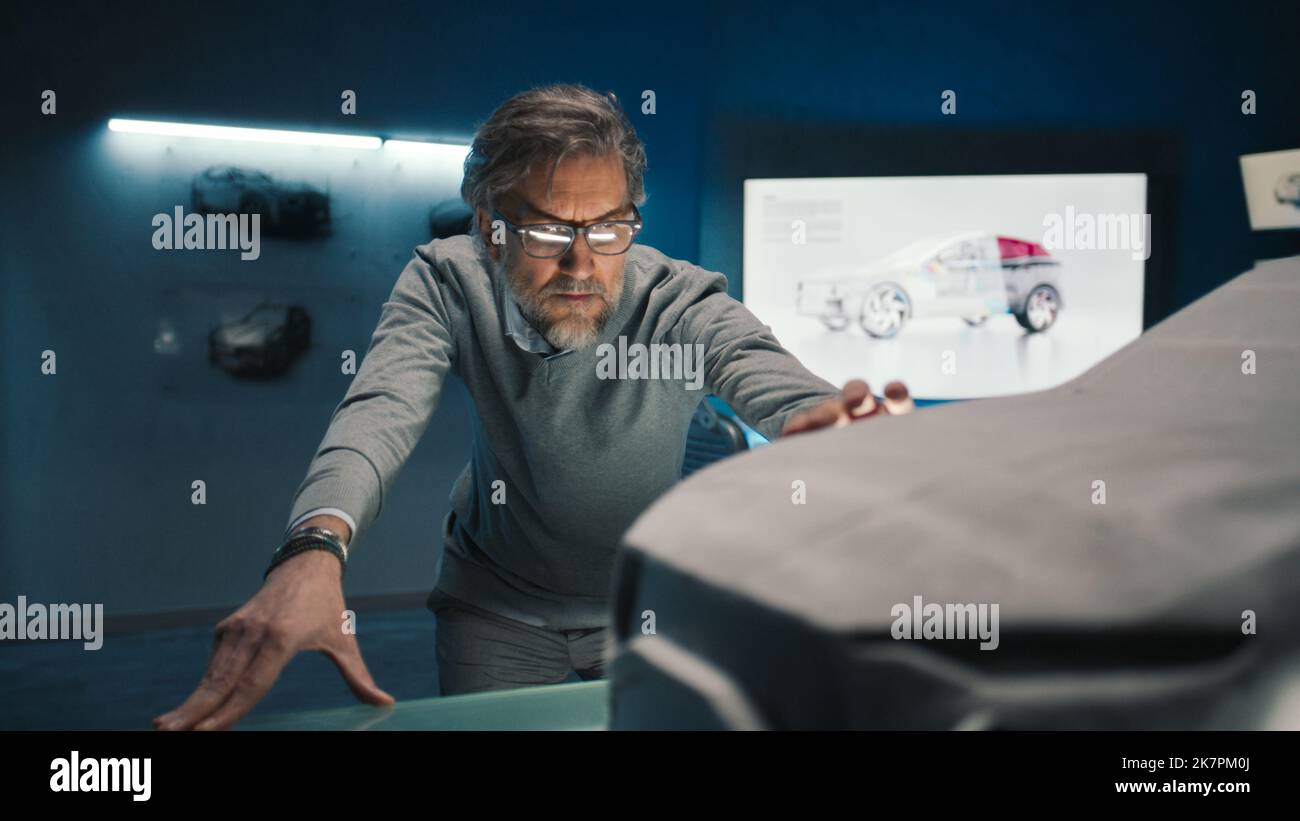 L'ingénieur automobile touche le modèle de la voiture prototype faite d'argile pour apporter des changements finaux dans la conception. Développeur de voitures à cheveux gris avec verres encadrés dans une entreprise de fabrication de voitures. Banque D'Images