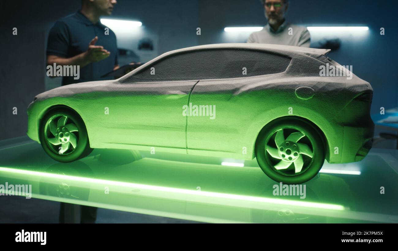 Des ingénieurs automobiles expérimentés examinent le modèle de voiture prototype dans différentes nuances de lumière pour choisir la couleur de la voiture future. Utilisation d'une application spéciale sur une tablette numérique et une table d'éclairage. Banque D'Images
