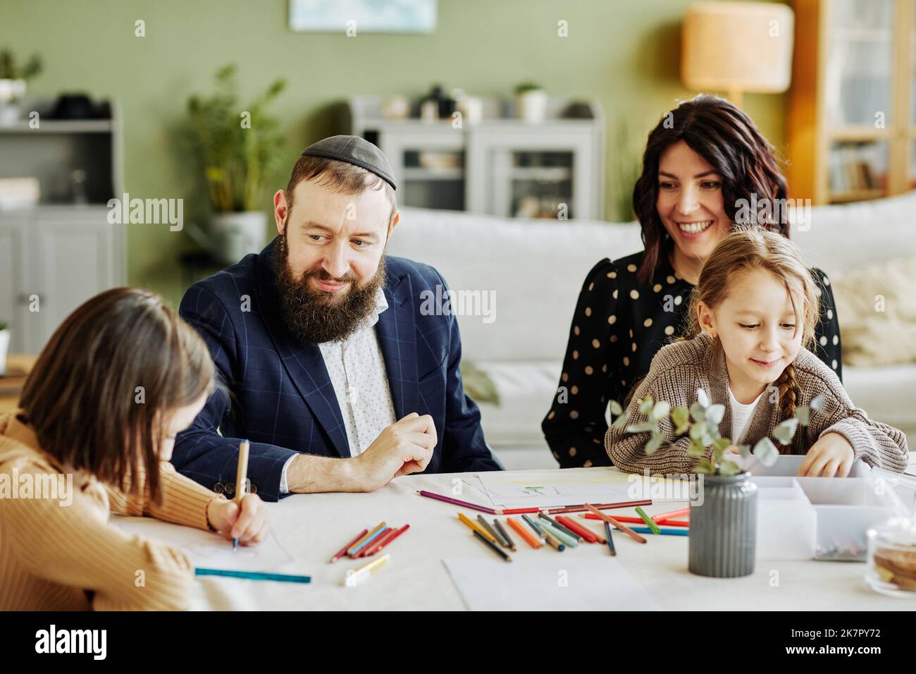 Portrait de la famille juive moderne en train de dessiner ensemble tout en étant assis à la table , se concentrer sur le sourire père portant le kippah Banque D'Images