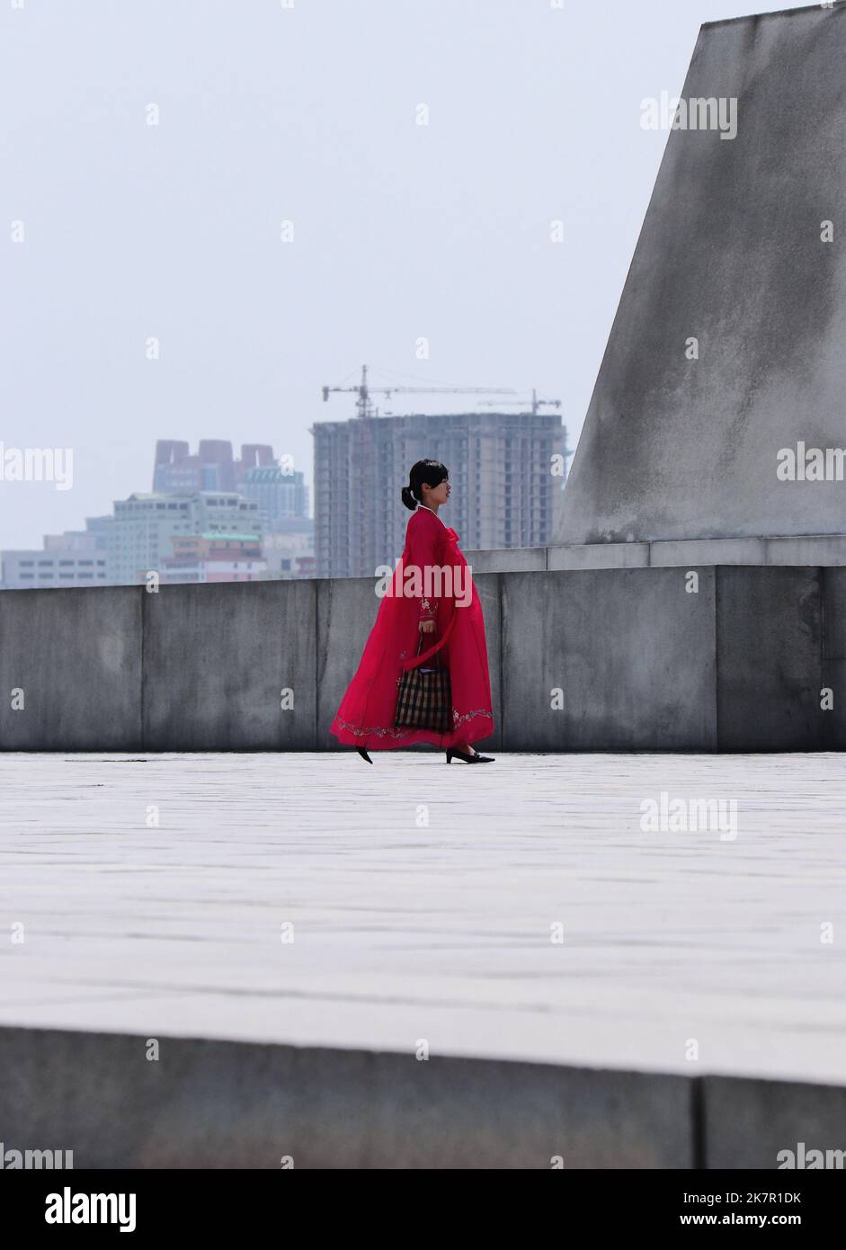 Une femme marche dans son hanbok traditionnel rose, la tenue nationale coréenne. L'architecture brutaliste est renforcée par l'utilisation approfondie du béton. Banque D'Images