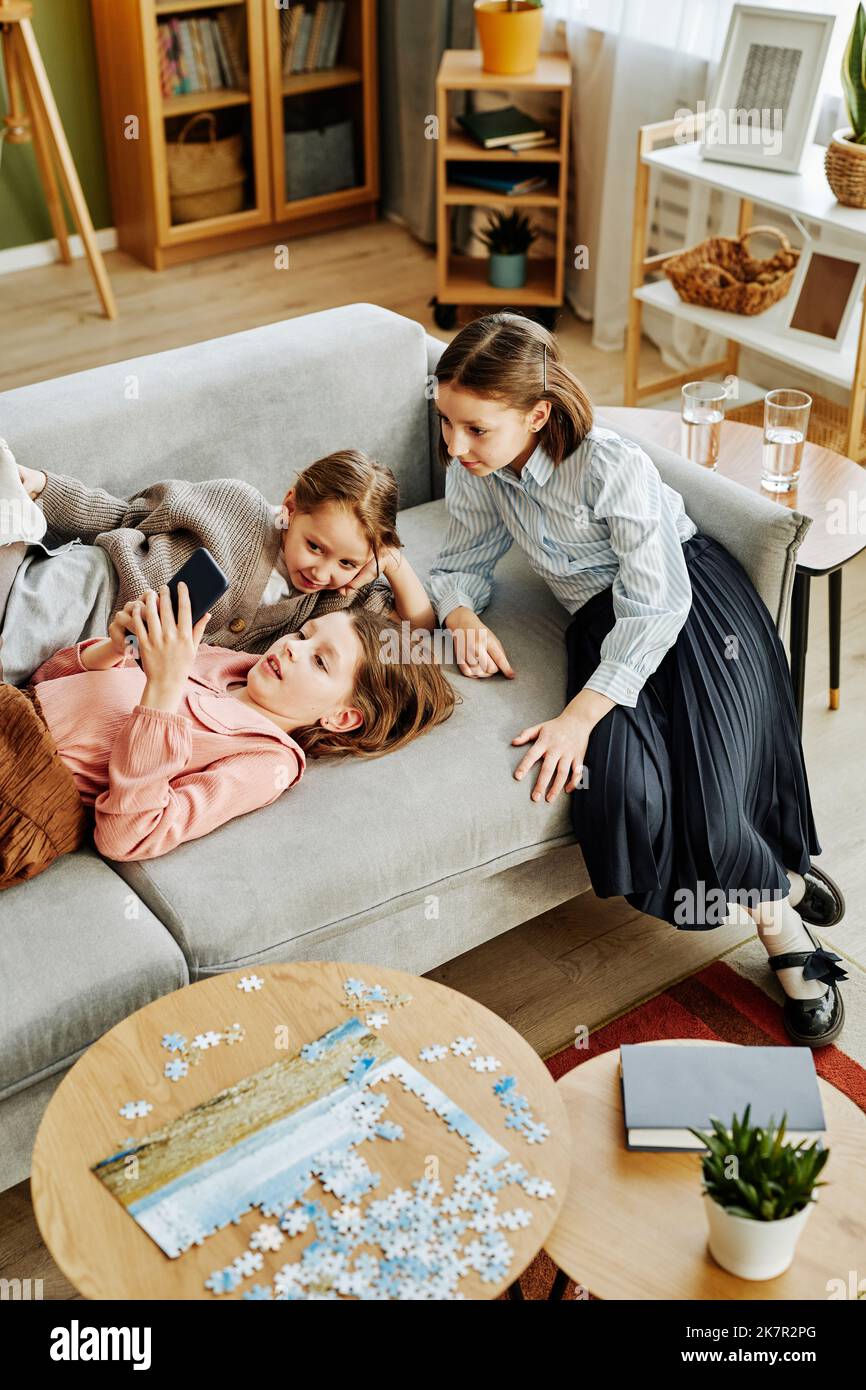 Vue en grand angle de trois petites filles jouant ensemble sur un canapé à la maison et à l'aide d'un smartphone Banque D'Images