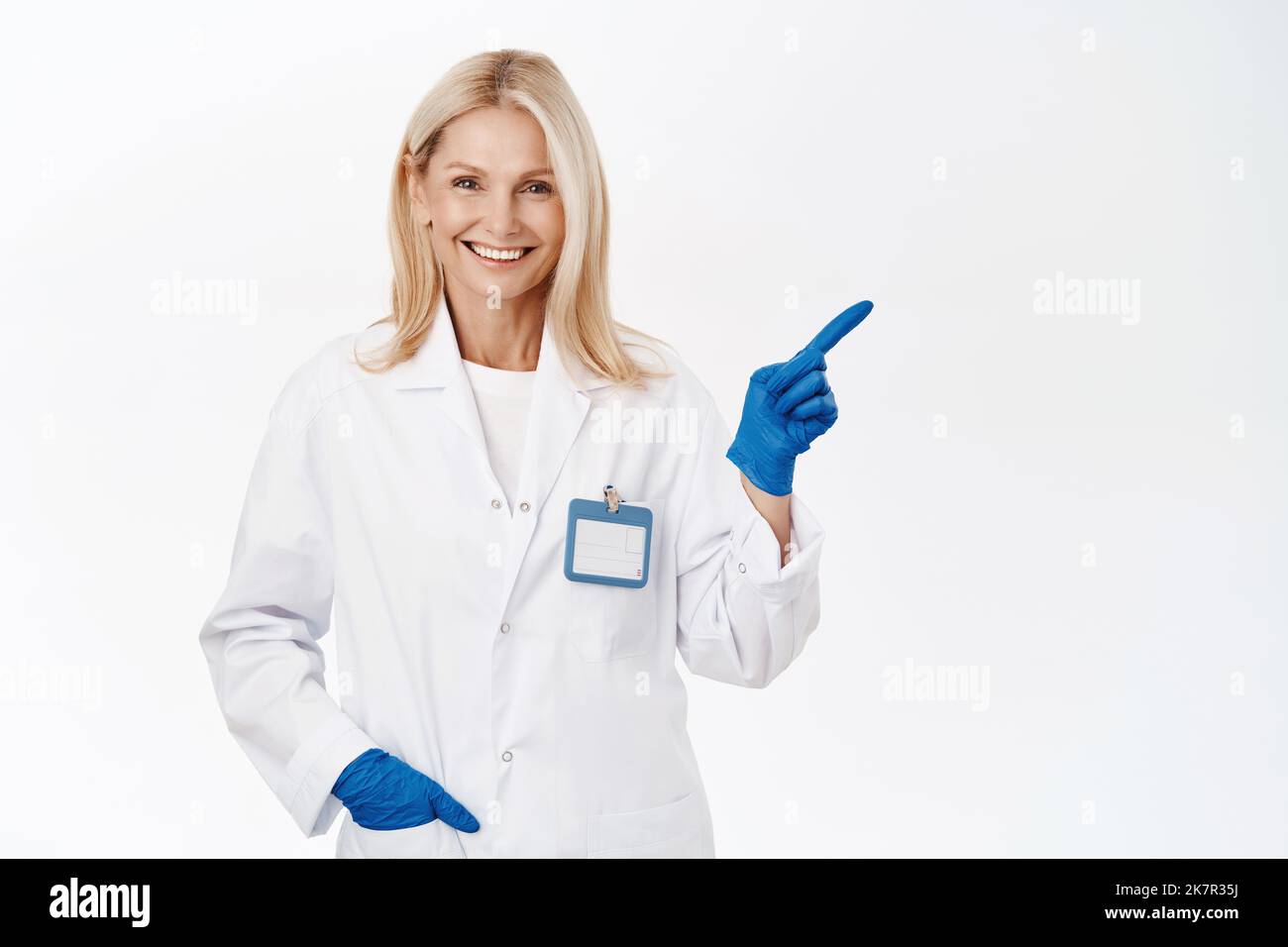 Sourire médecin dans les gants médicaux pointe à droite, montre la publicité, le logo de la clinique, se tient sur fond blanc Banque D'Images