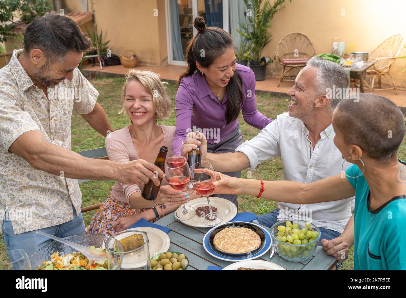 Un groupe d'amis joyeux qui se couguent avec un beau sourire autour de la table au patio de la maison. Banque D'Images