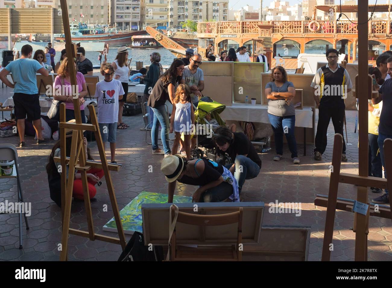Une foule et des médias variés lors d'une foire artistique en plein air à Dubaï, les Émirats arabes Unis regardent comme une artiste féminine peint une toile sur place. Un vidéaste masculin prend un gros plan. Banque D'Images