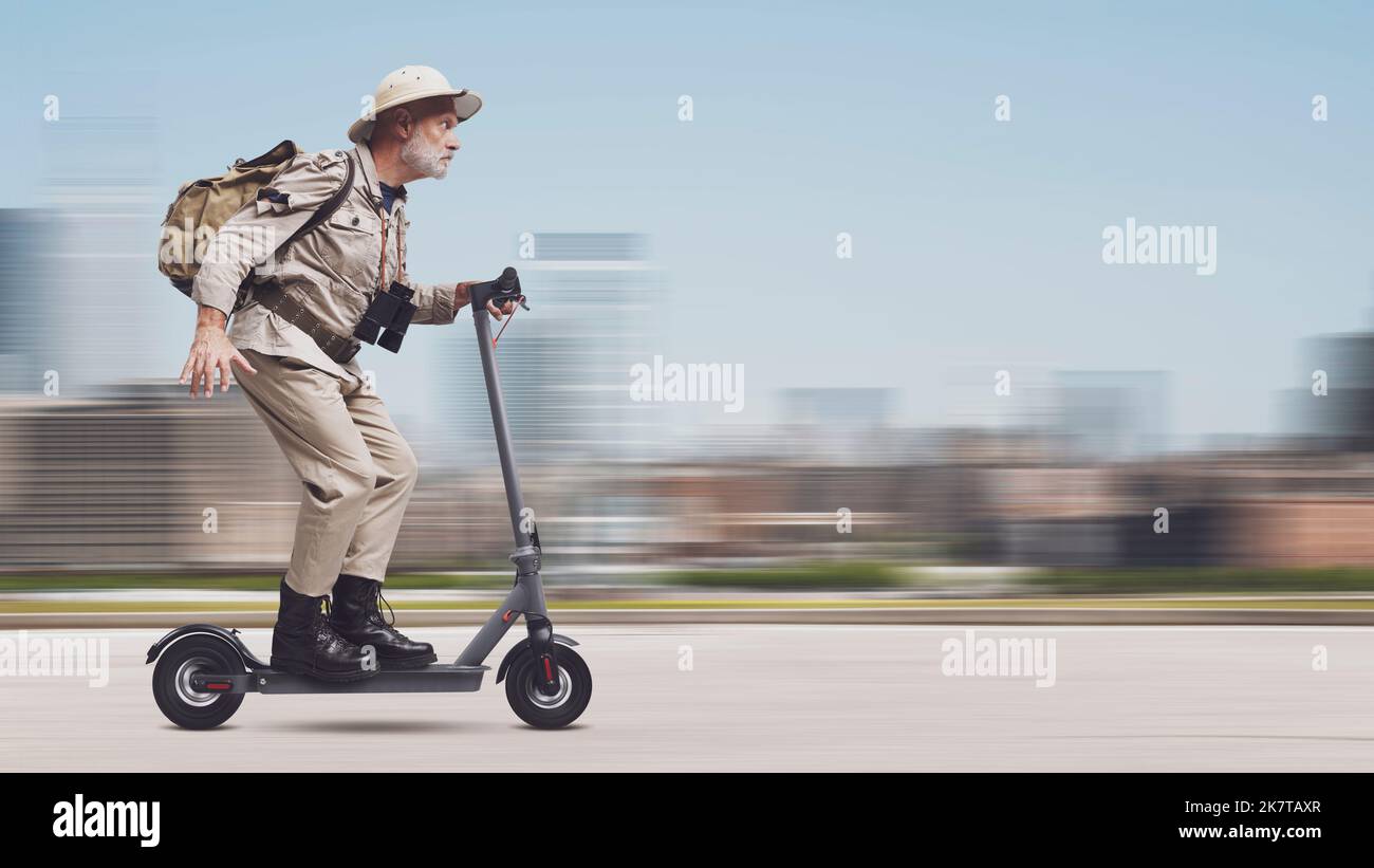 Drôle d'explorateur urbain senior à cheval sur un scooter électrique rapide dans la rue de la ville Banque D'Images