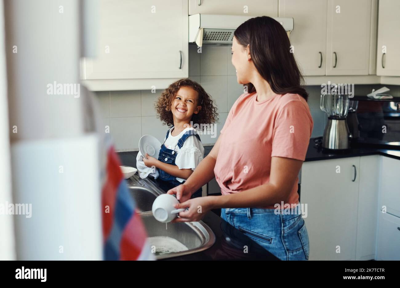Mon petit assistant. une adorable jeune fille debout et aidant sa mère avec les plats dans la cuisine à la maison. Banque D'Images