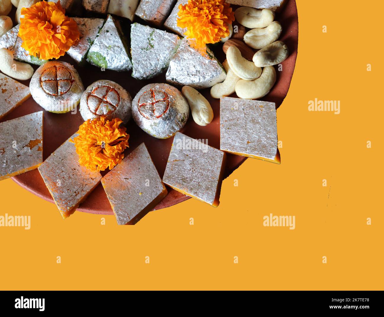 Assortiment de bonbons indiens/fruits secs/fleurs marigold dans une assiette en terre cuite/argile sur fond jaune/festival Diwali/Deepavali Banque D'Images