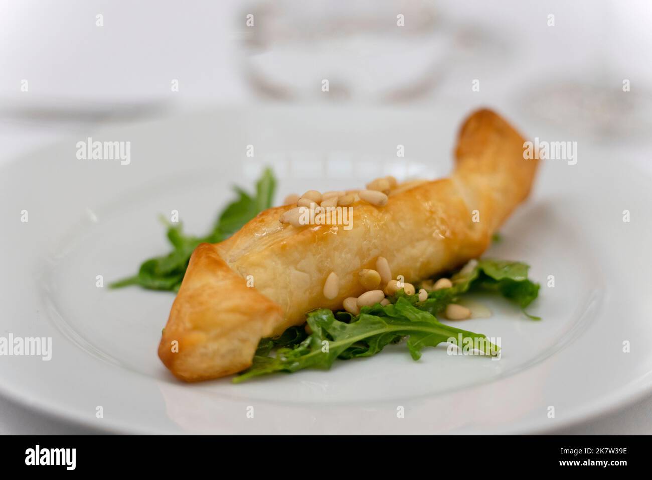 Plat gastronomique élégamment plaqué avec un rouleau de pâte feuilleté brun doré sur un lit de feuilles de roquette vertes fraîches garnies de pignons de pin Banque D'Images