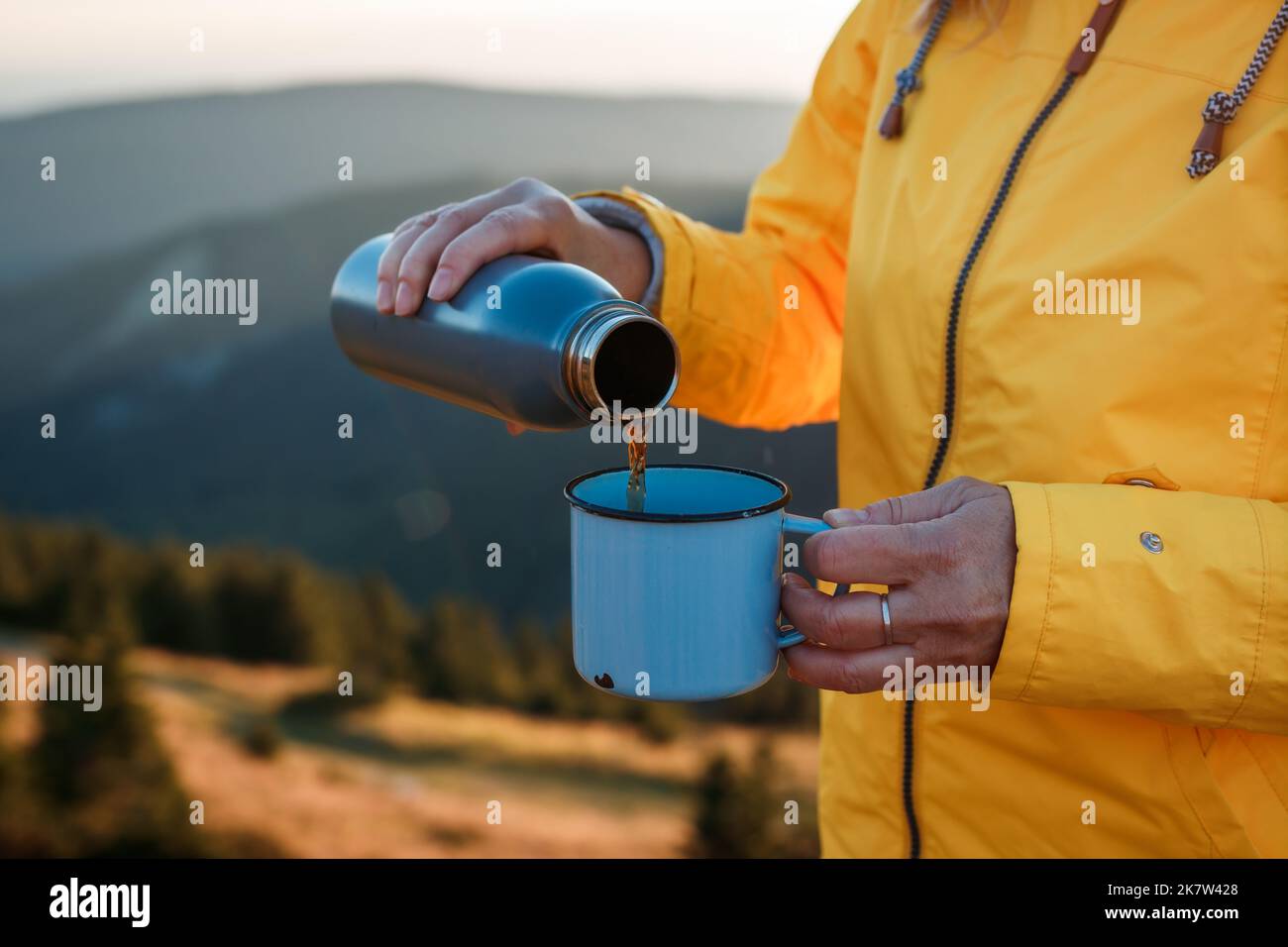 Le randonneur verse une boisson chaude du thermos dans une tasse de voyage dans les montagnes. Rafraîchissements pendant le trek Banque D'Images