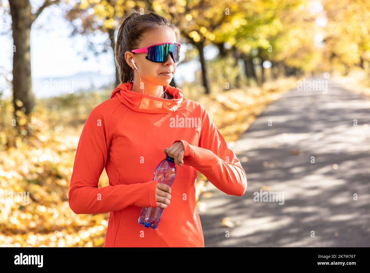 Une jeune femme portant des écouteurs ouvre une bouteille d'eau à l'extérieur après l'entraînement cardio. Banque D'Images
