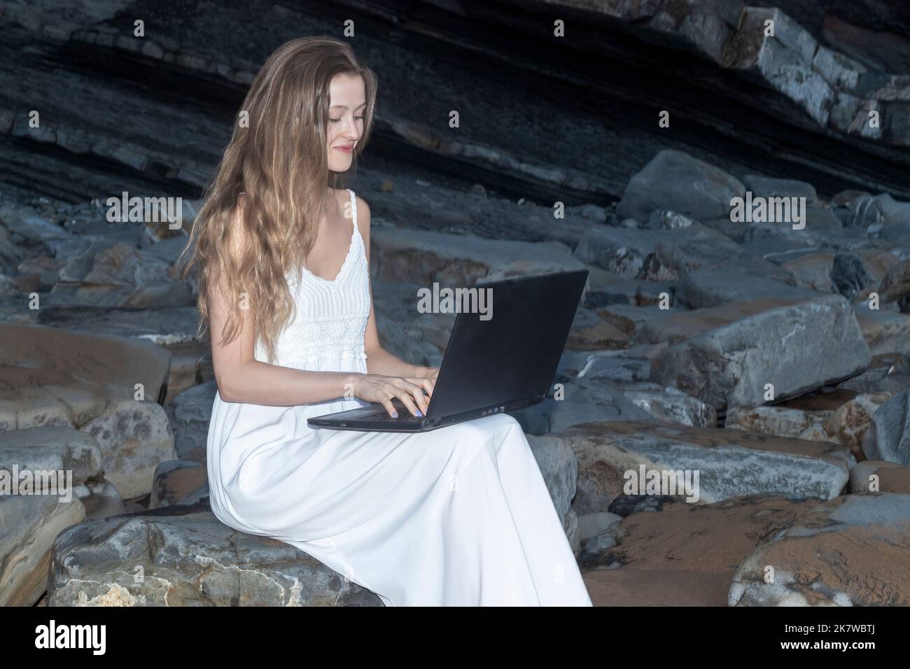 Une femme utilisant et tapant sur le clavier d'ordinateur portable tout en étant assise sur une belle plage Banque D'Images