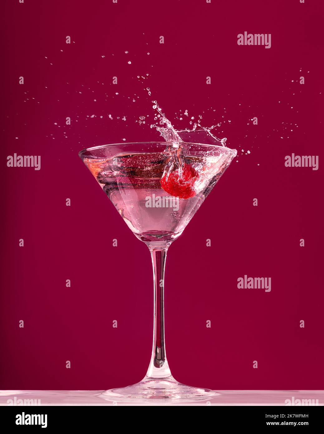 Framboise éclabousse dans un verre à cocktail martini sur fond rouge foncé Banque D'Images
