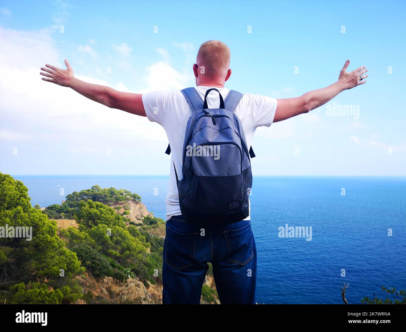 Photo panoramique d'un homme heureux aux bras étirés, qui a conquis le pic de la vie avec une belle vue sur la mer et la côte rocheuse. Le Banque D'Images