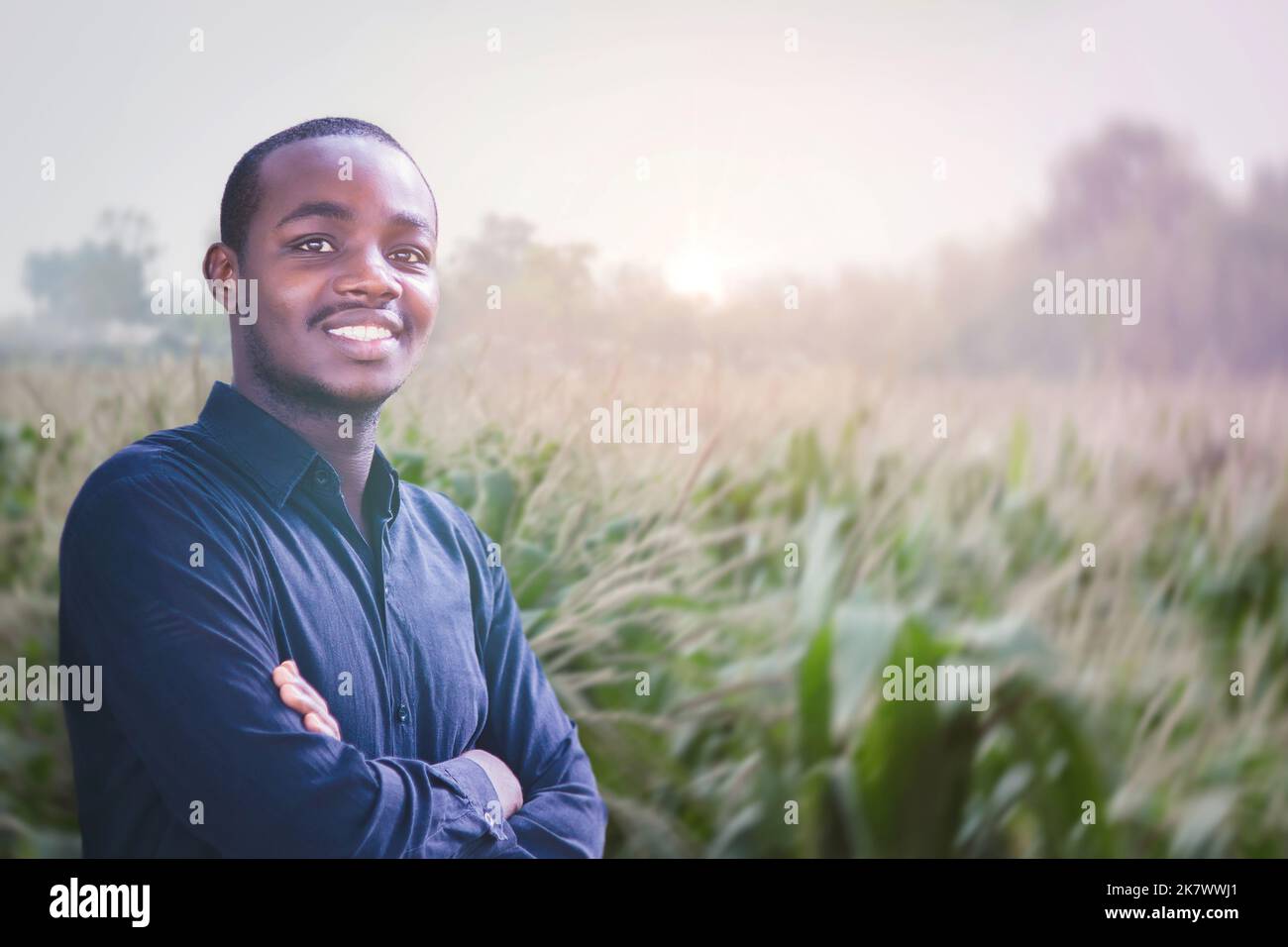 Portrait d'un fermier africain debout dans le champ au coucher du soleil avec sourire à l'appareil photo Banque D'Images