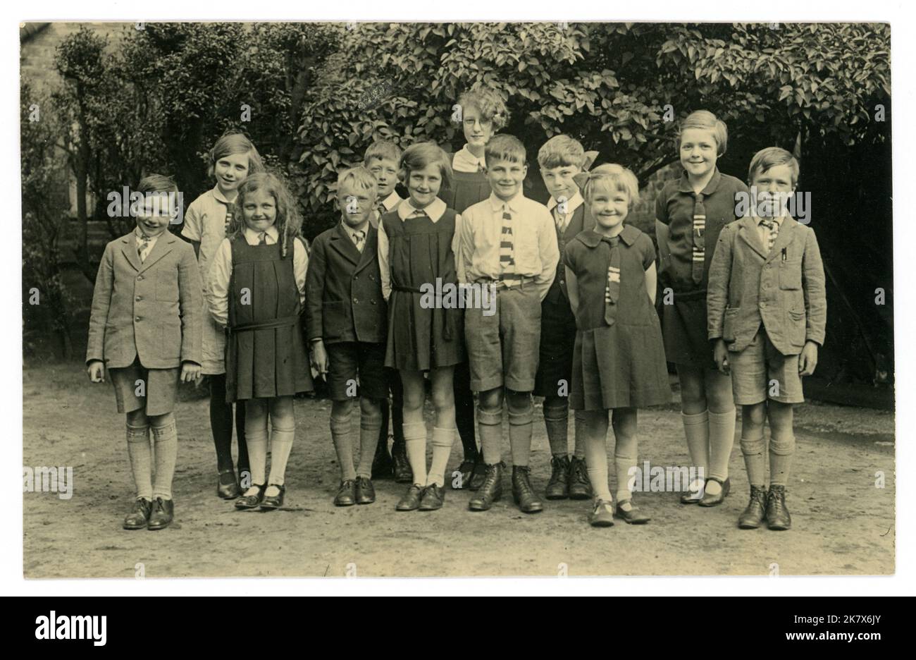 Original, très clair, carte postale, de l'ère WW2, années 1920, l'ère des années 1930 de groupe d'écoliers smling portant un uniforme scolaire intelligent, avec des cols, des cravates, des tuniques plissées de boîte, des vestes et des shorts, posant pour une photographie dans leur uniforme scolaire à l'extérieur dans la cour de récréation. Quelques personnages. ROYAUME-UNI Banque D'Images