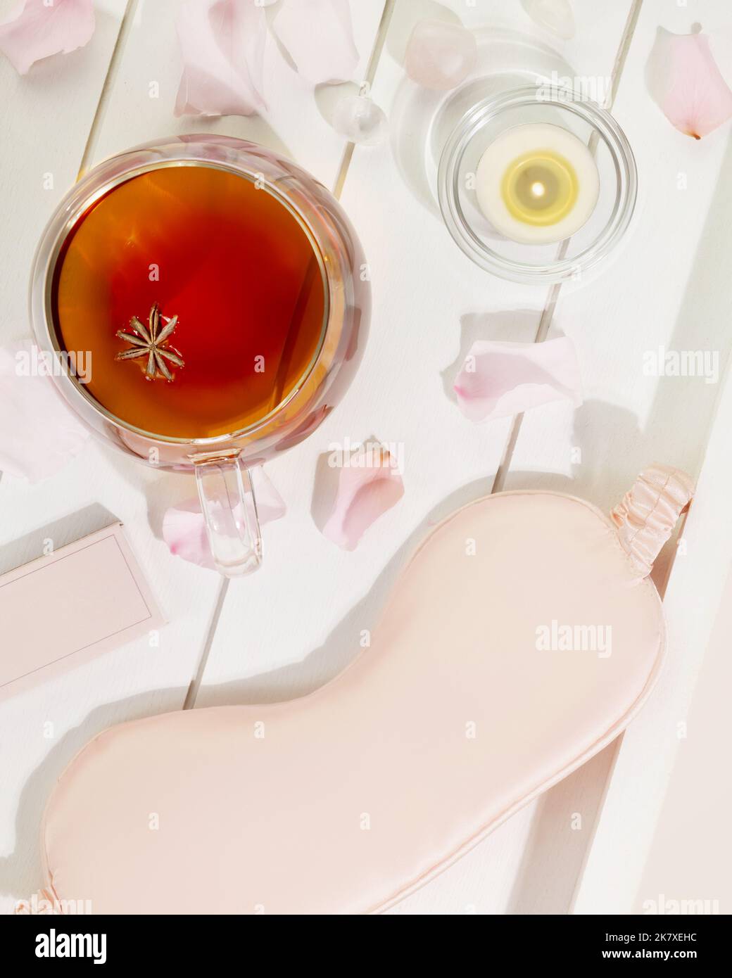 Masque de sommeil, tasse de thé, bougie et pétales de rose sur un plateau en bois blanc Banque D'Images