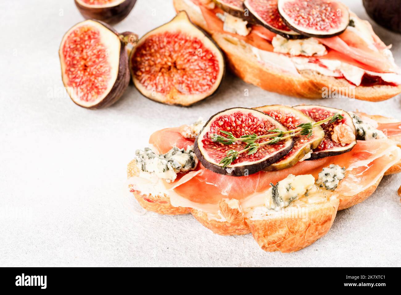Bruschetta croissant frais avec figue mûre, fromage bleu, prosciutto, noix et herbes sur fond de table en béton blanc. Mise au point sélective Banque D'Images