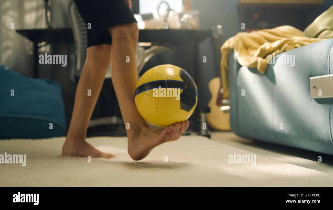 Garçon joue au football sur le tapis seul dans sa chambre. Coup de pied sur le ballon. Préparation du match de football de l'école. Sports, football, loisirs, concept de passe-temps. Banque D'Images