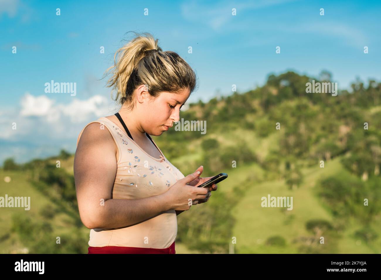 belle jeune latina femme, au sommet d'une montagne avec son téléphone portable dans la main, en interaction sur les réseaux sociaux, à la recherche d'informations avec le h Banque D'Images