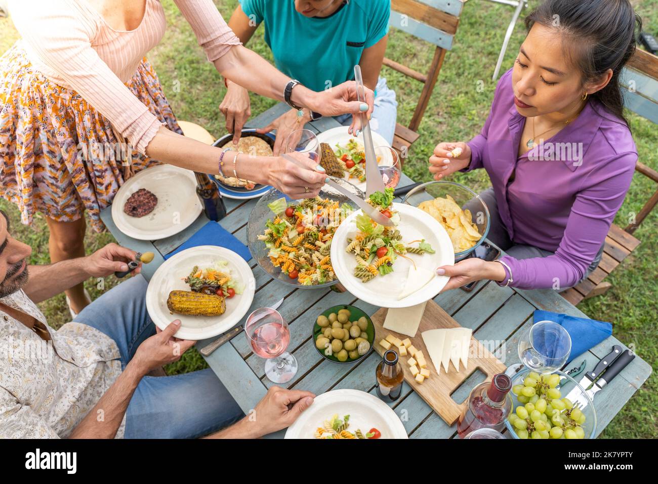 Des amis heureux rient avec un grand sourire autour de la table dans un dîner d'été. La femme sert la nourriture dans le patio de la maison. Sourires, gaieté concept. Banque D'Images