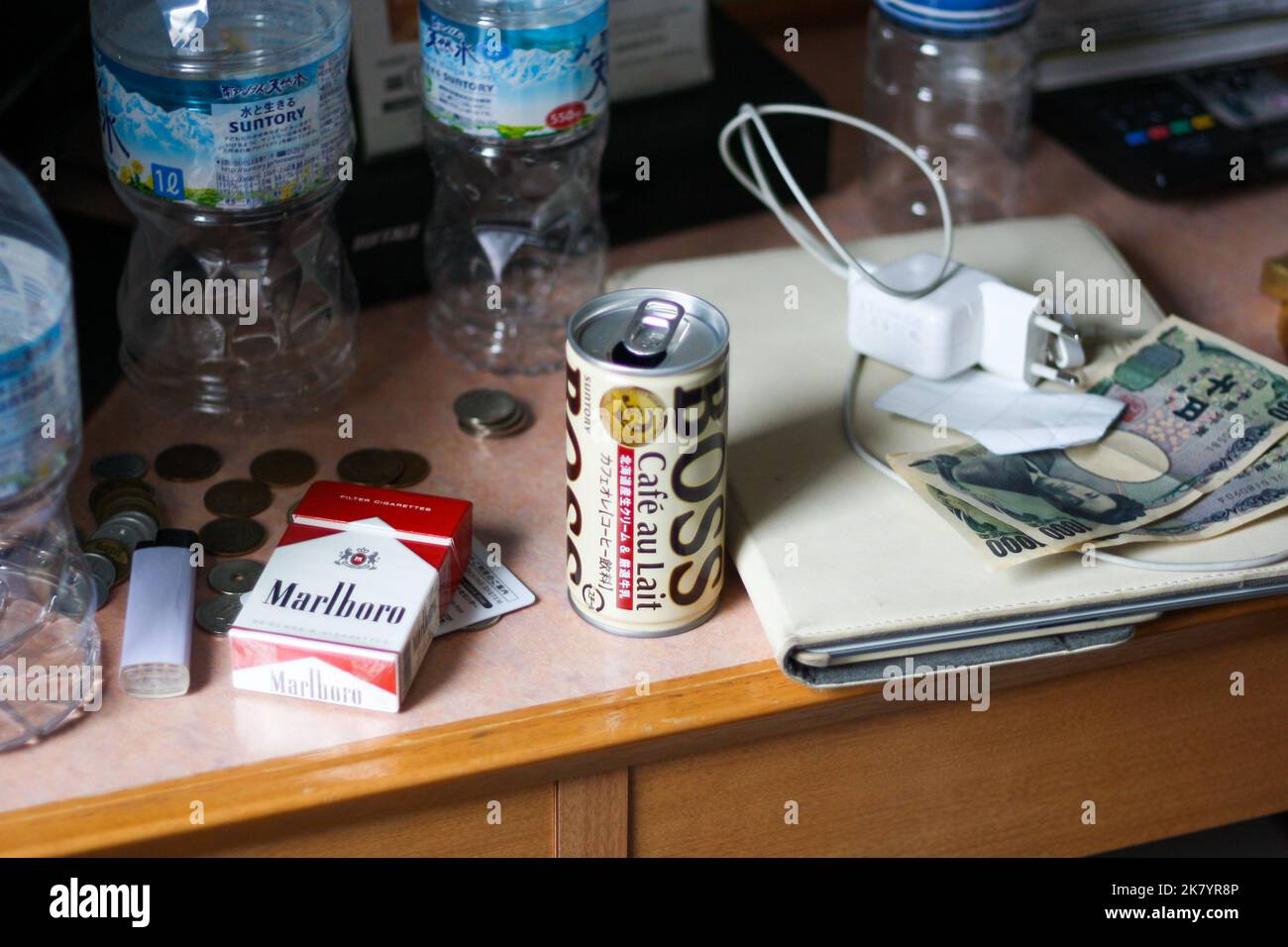 Petit bureau en bois désordonné dans la chambre d'hôtel avec bouteilles d'eau en plastique, billets et pièces japonais, paquet de cigarettes, café en conserve et chargeur. Banque D'Images