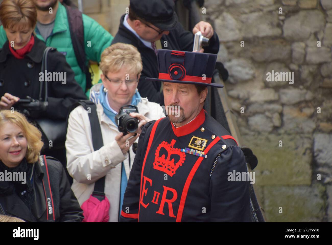 Yeoman de la Garde en uniforme donne une visite guidée de la Tour de Londres aux touristes qui tiennent des caméras Banque D'Images