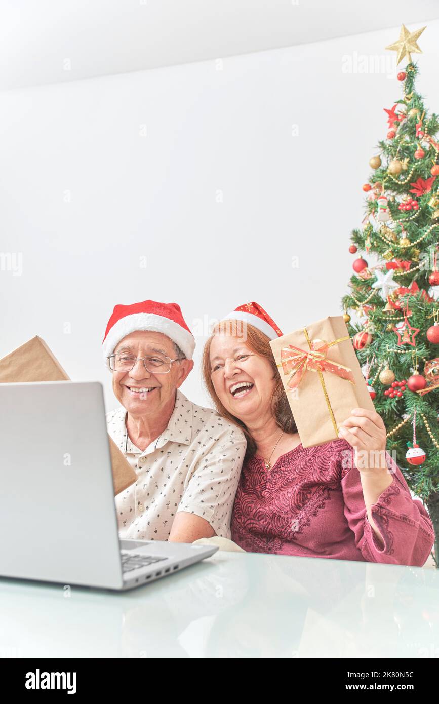 Un couple latin senior a accueilli ses proches par appel vidéo à Noël, leur montrant leurs cadeaux. Concepts: La joie de partager pendant les vacances, le Banque D'Images