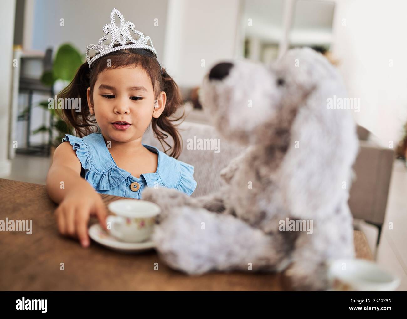 Fille, jouet et thé à une table avec une couronne de princesse, jouer, s'amuser et parler dans sa maison. Fantaisie, créatif et fille regardant heureux pendant Banque D'Images