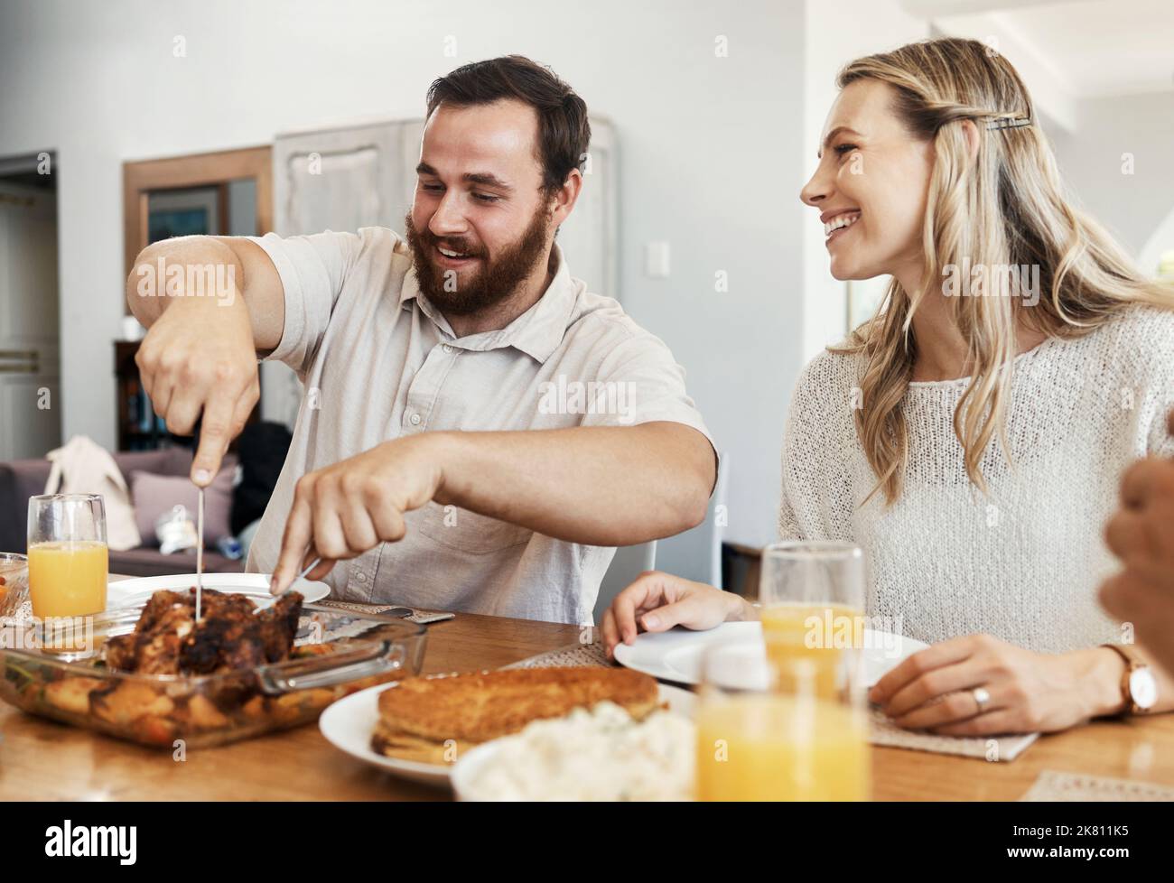 Famille, nourriture et homme coupant du poulet au dîner avec une femme souriant, mangeant et buvant ensemble dans la salle à manger. Heureux, attention et célébrer, partager Banque D'Images
