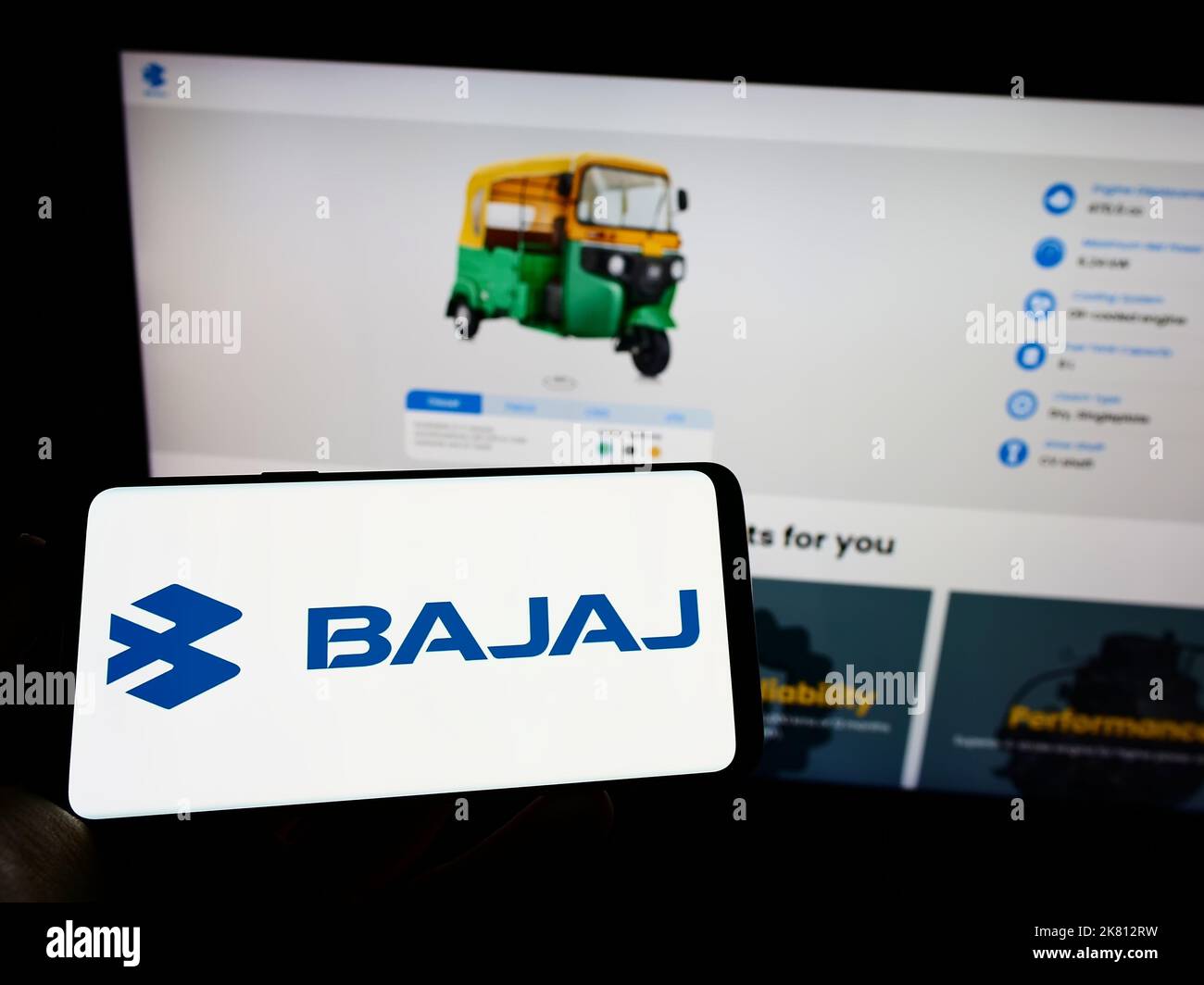 Personne tenant un téléphone portable avec le logo de la compagnie automobile indienne Bajaj Auto Limited à l'écran en face de la page Web d'affaires. Mise au point sur l'affichage du téléphone. Banque D'Images