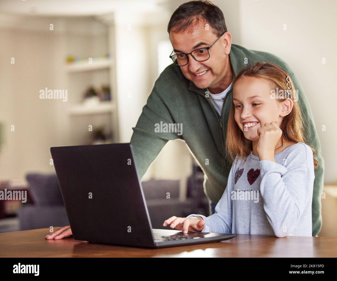 J'ai gagné le niveau. Une adorable petite fille assise et utilisant un ordinateur portable à la maison tandis que son père l'aide. Banque D'Images