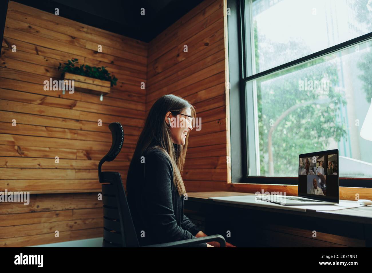 Bonne jeune femme d'affaires ayant un appel vidéo dans un espace de travail moderne. Jeune femme d'affaires gaie communiquant avec ses associés d'affaires wh Banque D'Images
