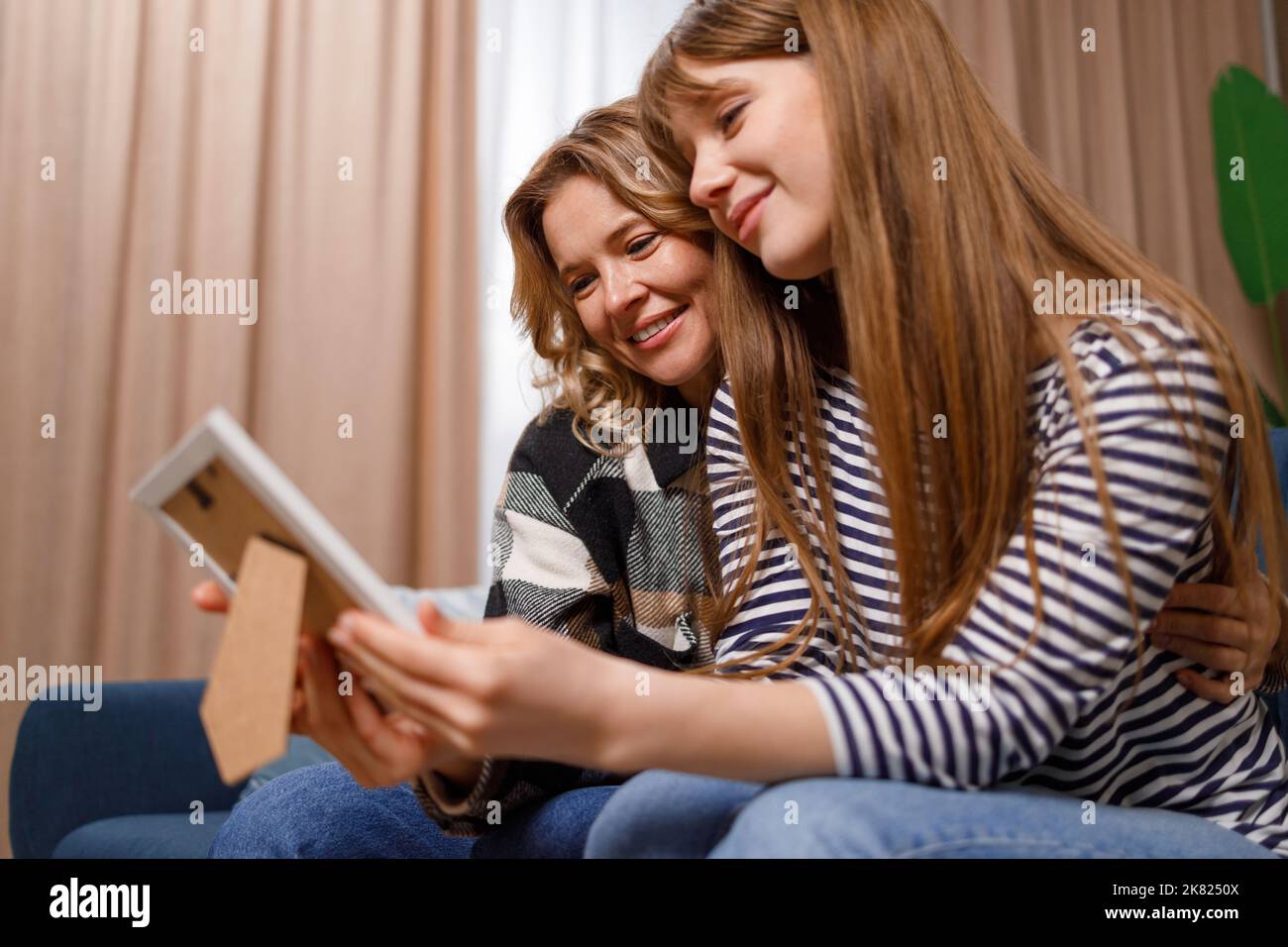 Une jeune femme qui visite sa mère est assise sur le canapé et regarde une photo dans un cadre. Maman et fille regardant de vieilles photos Banque D'Images