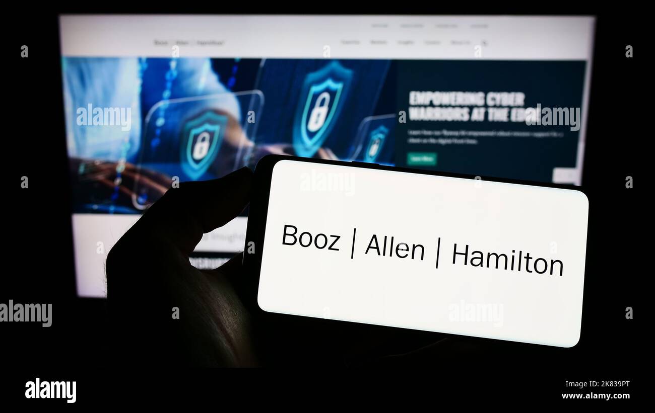 Personne tenant un téléphone portable avec le logo de la société américaine de conseil Booz Allen Hamilton Inc. À l'écran devant la page Web. Mise au point sur l'affichage du téléphone. Banque D'Images