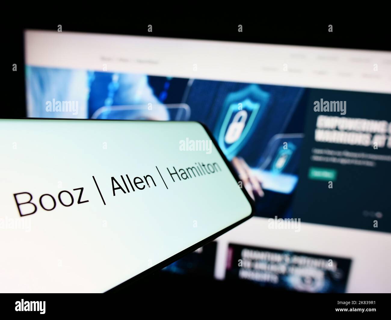 Téléphone portable avec logo de la société de conseil américaine Booz Allen Hamilton Inc. À l'écran devant le site Web. Mise au point au centre-gauche de l'écran du téléphone. Banque D'Images
