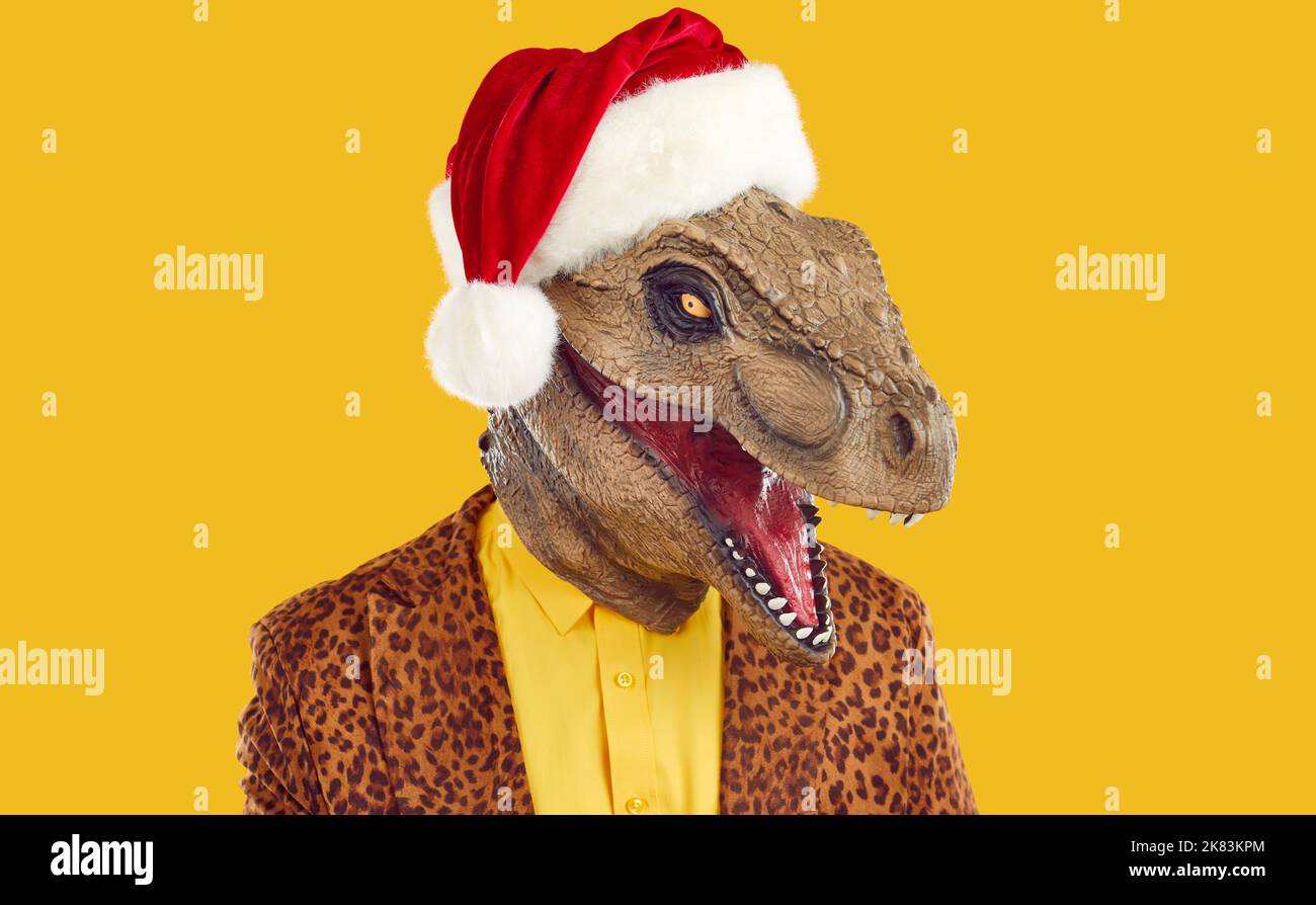 Homme dans un drôle masque de dinosaure, chapeau de Noël rouge et veste de léopard isolée sur fond jaune Banque D'Images