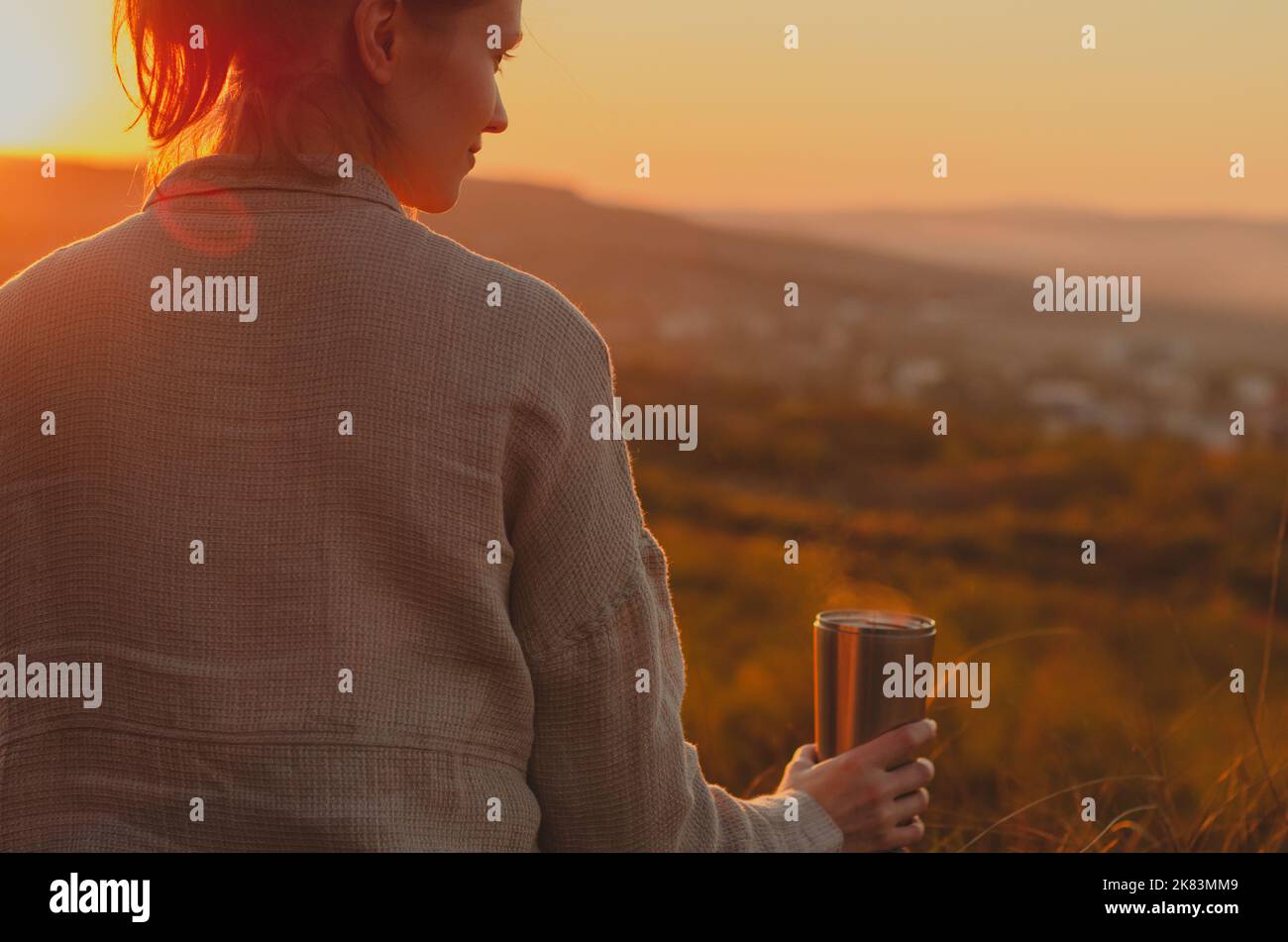 Vue arrière de la femme en train de prendre un thé chaud sur la colline au coucher du soleil Banque D'Images