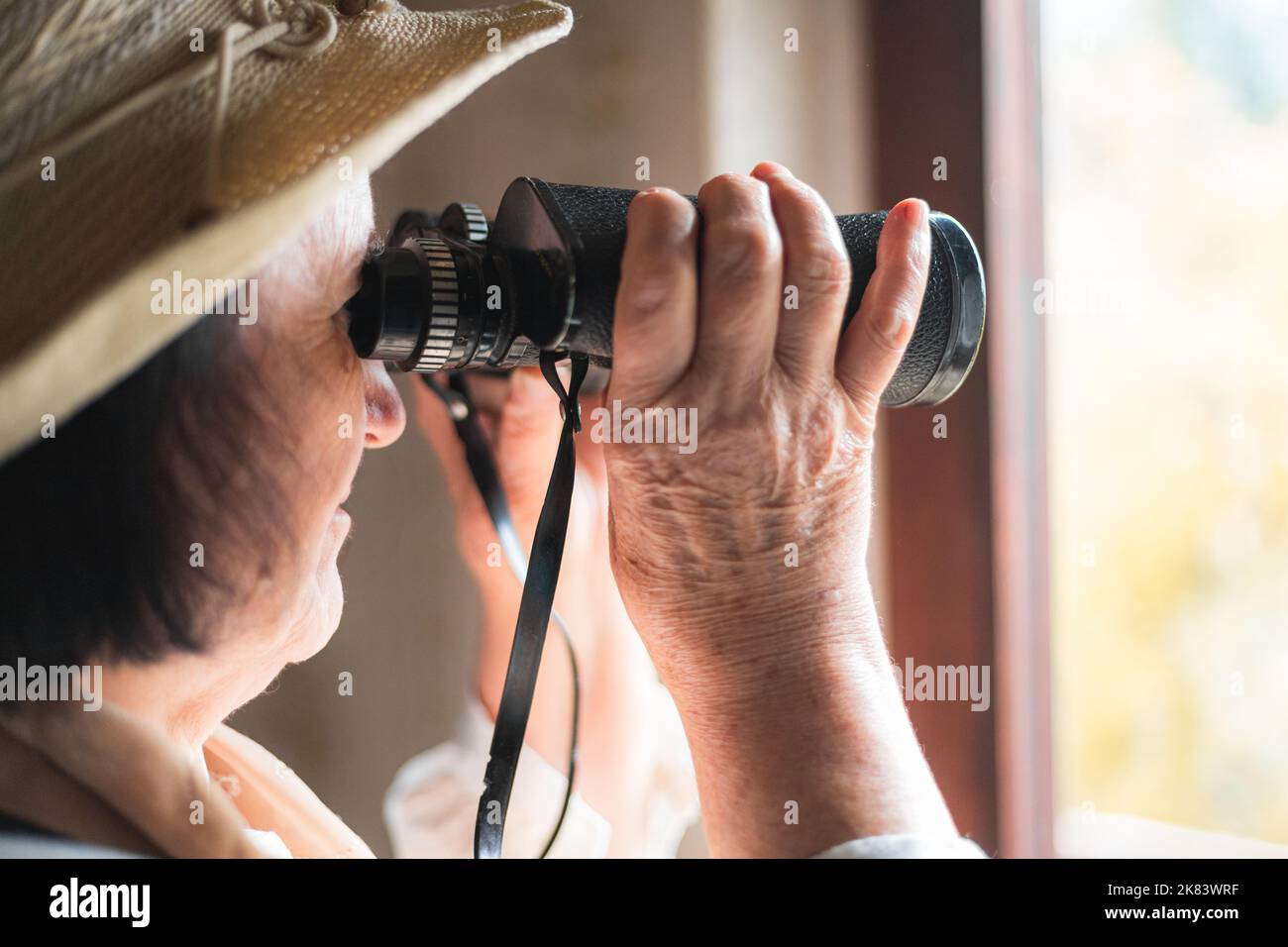 Femme âgée regardant à travers les jumelles, l'espionnage Banque D'Images
