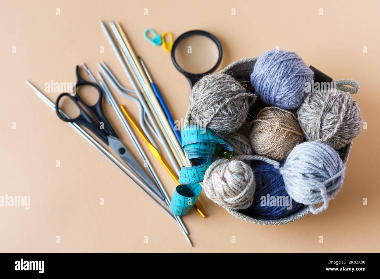 Accessoires de tricotage, crochet, aiguilles, ciseaux, loupe, centimètre, un panier avec des boules de fil bleu gris brun sur fond orange. Banque D'Images