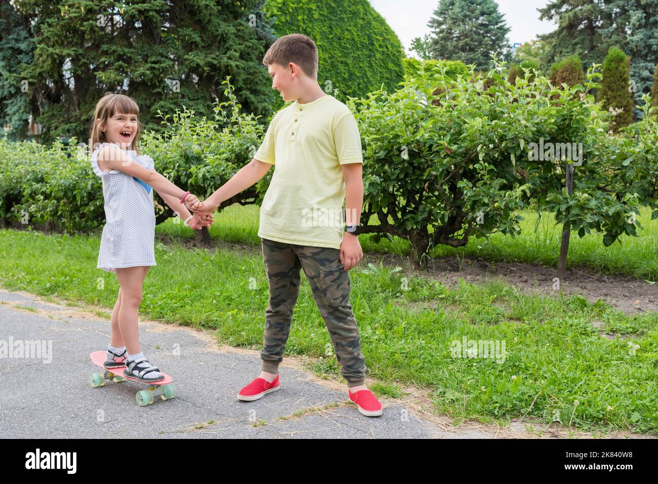 Un garçon enseigne à une fille le skateboard dans un parc, en tenant sa main. Un mode de vie sain Banque D'Images
