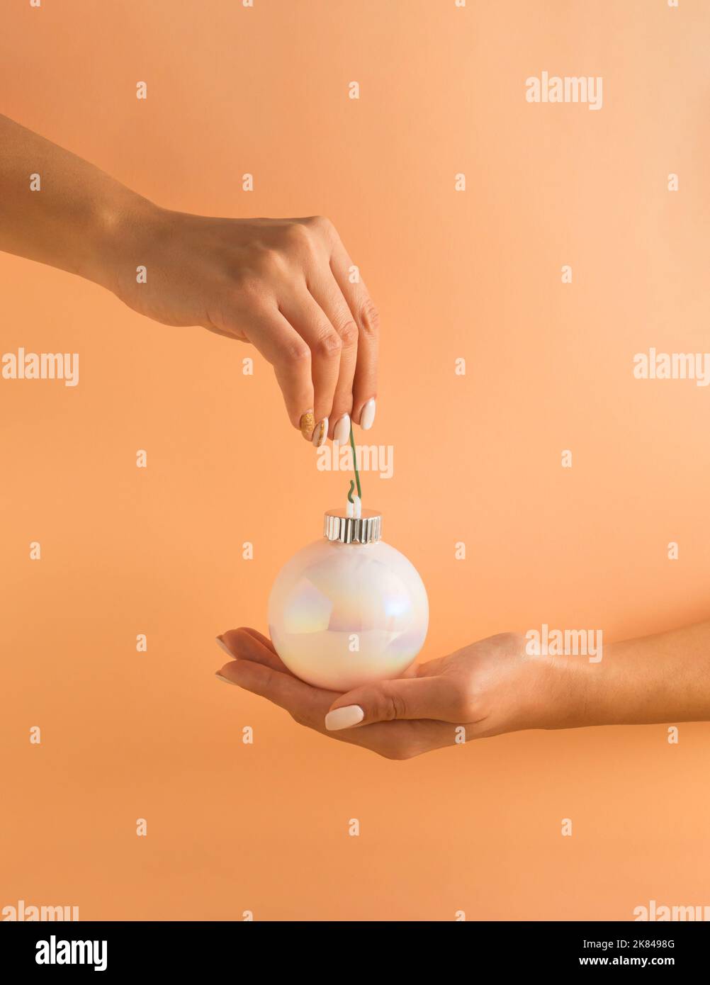 Mains de femme tenant blanc brillant boule de Noël sur fond orange pastel. Concept de vacances minimal. Bonne Année. Banque D'Images