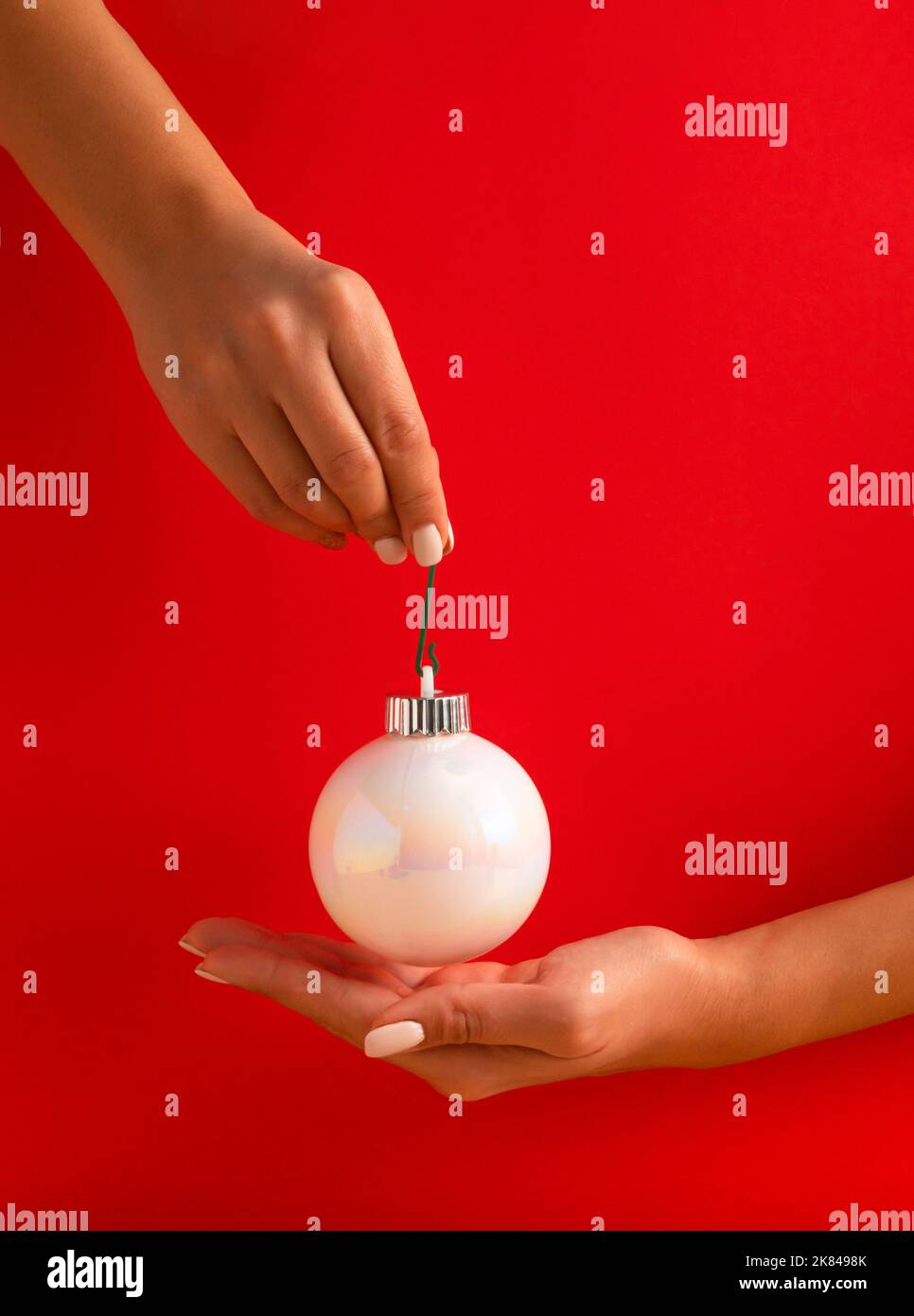 Mains de femme tenant blanc brillant boule de Noël sur fond rouge. Concept de vacances minimal. Bonne Année. Banque D'Images