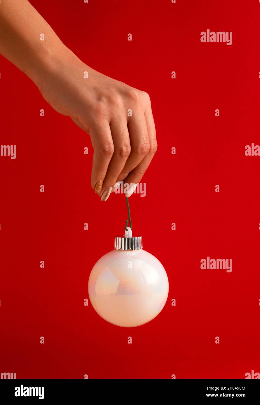 Main de femme tenant une boule de Noël blanche brillante sur fond rouge. Concept de vacances minimal. Bonne Année. Banque D'Images