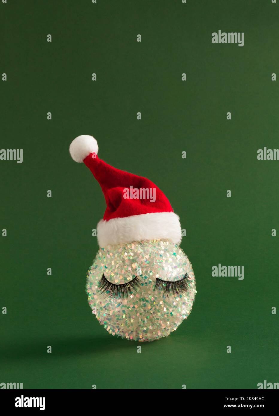 Boule de Noël blanche brillante avec cils et chapeau de Père Noël sur fond vert vif. Bonne année de fond. Banque D'Images