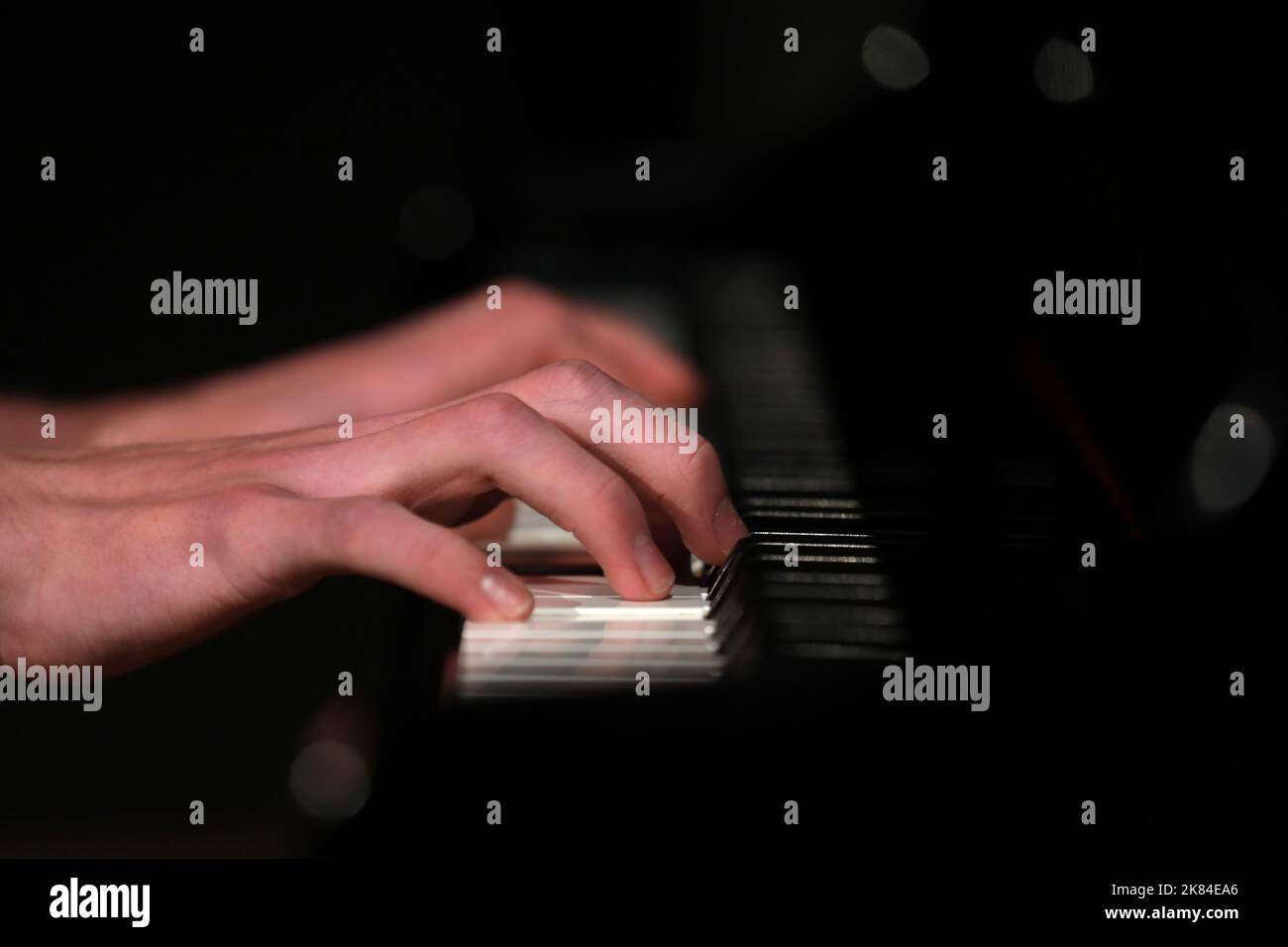 Gros plan d'un pianiste mains et doigts jouant les touches sur un piano. Isolé contre un arrière-plan noirci avec des lumières floues et de la réflectio Banque D'Images