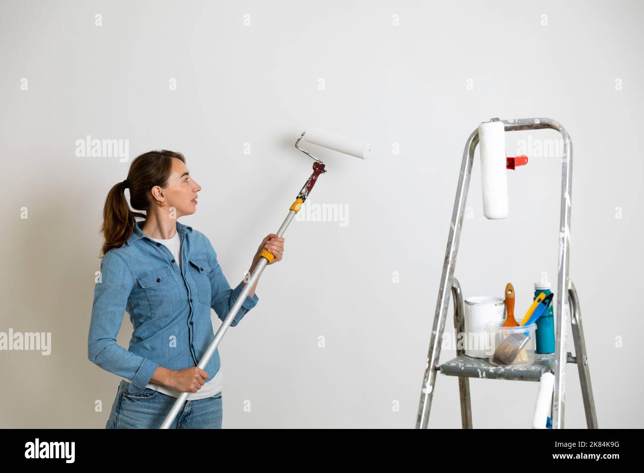 Femmes tenant un rouleau de peinture pour colorer les murs, échelle avec des pinceaux et des outils. Concept d'amélioration de la maison. Banque D'Images