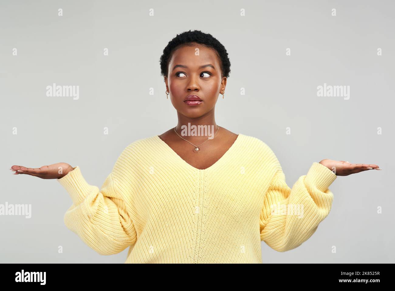 J'ai besoin que vous choisissiez... une jeune femme qui tient ses mains tout en se tenant debout sur un fond gris. Banque D'Images