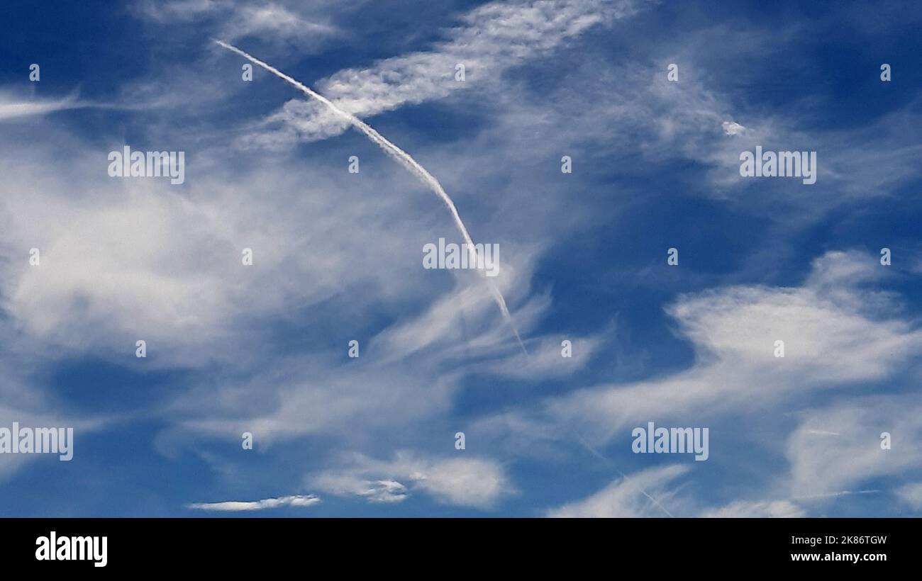 Nuages dans un ciel légèrement fou d'été, le sillage d'un avion de passage déformé par le vent forme une grande virgule Banque D'Images