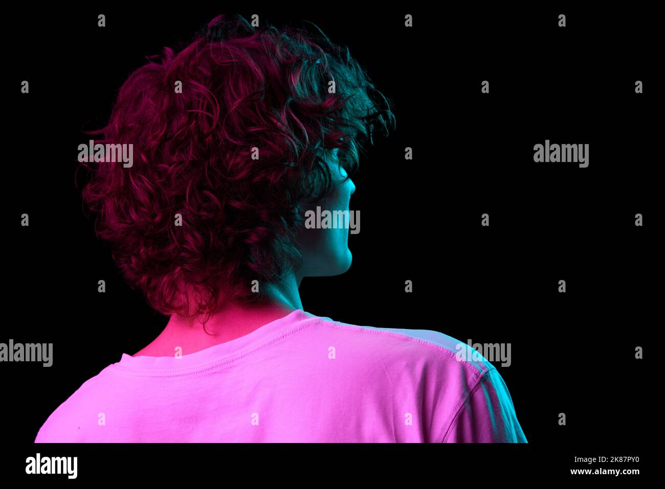 Vue arrière d'un jeune homme poilu, étudiant en t-shirt blanc isolé sur fond sombre dans la lumière néon. Concept des émotions, expression faciale, jeunesse Banque D'Images